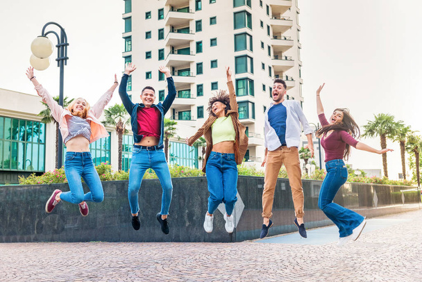 Gruppo di giovani amici esuberanti e diversi che saltano in aria in una strada della città acclamando e ridendo con gioia mentre festeggiano insieme - Foto, immagini