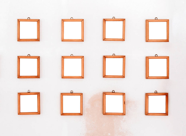 Zwölf leere kleine quadratische Holzrahmen an einer weißen Wand mit rötlich verfärbtem Fleck unten in drei Reihen bereit für eine Show oder Ausstellung - Foto, Bild