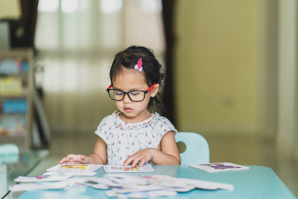 A cute little Asian girl wearing eyeglasses playing jigsaw puzzle at home - Фото, изображение