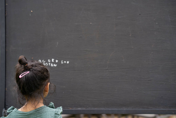 A back view of a cute little Thai girl writing the alphabet on a blackboard - Foto, Imagem
