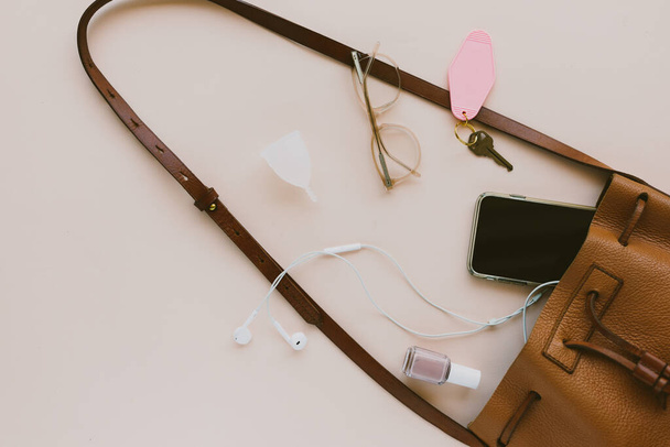 A top view of the contents of a woman's purse spilling out on a pink background - 写真・画像