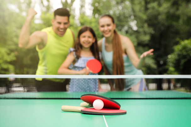 Family near ping pong table in park, focus on rackets and ball - Фото, зображення
