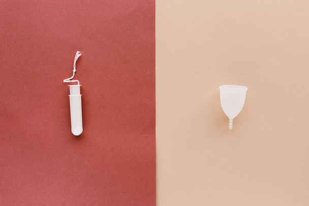 A menstrual cup and a tampon on a red and peach background - Fotoğraf, Görsel