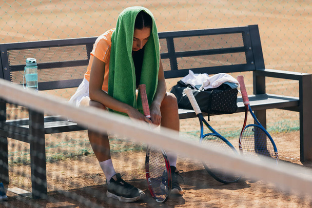 Žena tenista odpočívá na lavičce po aktivní hře na tenisovém kurtu - Fotografie, Obrázek