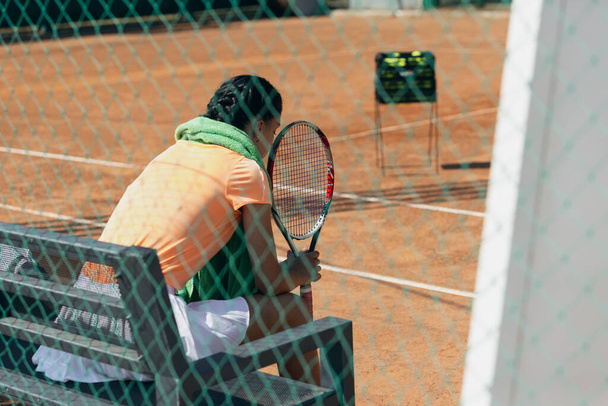 Zadní obraz ženského tenistky odpočívající na lavičce po aktivní hře na tenisovém kurtu - Fotografie, Obrázek