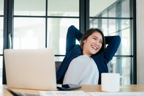 頭の後ろの快適なオフィスチェアの手でリラックスした穏やかな笑顔のビジネスマン女性,仕事が終わった後に満足オフィスで休んで幸せな女性 - 写真・画像