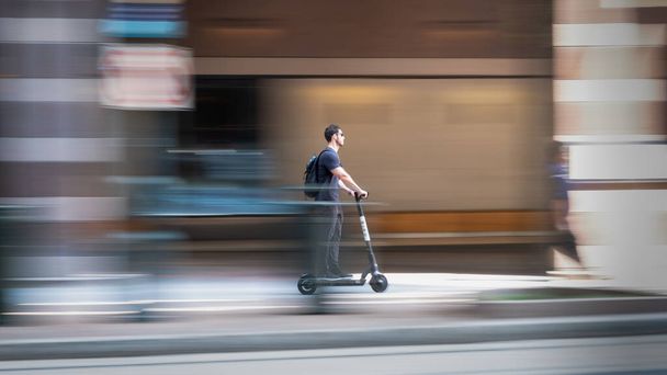 Charlotte, North Carolina, USA - August 24, 2021: Man with sunglasses rides scooter on sidewalk. - Φωτογραφία, εικόνα