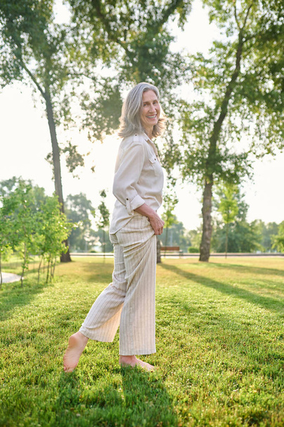 Joyful elegant woman standing barefoot on grass - Фото, изображение