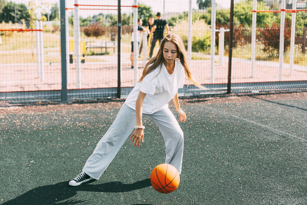 Teini-ikäinen tyttö johtaa koripalloa urheilukentällä, tyttö suojaa palloa pelin aikana. - Valokuva, kuva