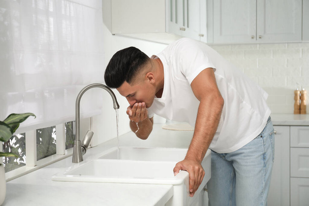 Man drinking tap water over sink in kitchen - 写真・画像