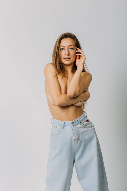 a young beautiful girl, with good body shapes, topless and in jeans, in the studio on a white background, with emotions on her face - Foto, imagen