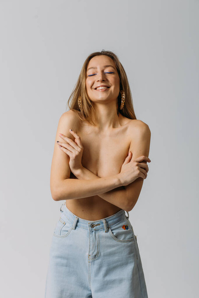 a young beautiful girl, with good body shapes, topless and in jeans, in the studio on a white background, with emotions on her face - Photo, Image