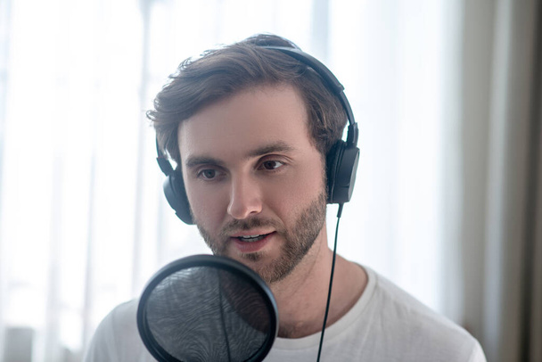 Young bearded man sitting in headphones and having an audio conference - Foto, imagen