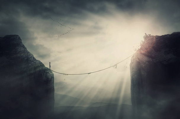 Person on the edge of precipice determined to overcome the obstacle by passing an old slackline bridge. The pursuit of success, danger and risk concept. Tightrope between two peaks, metaphoric scene - Photo, Image