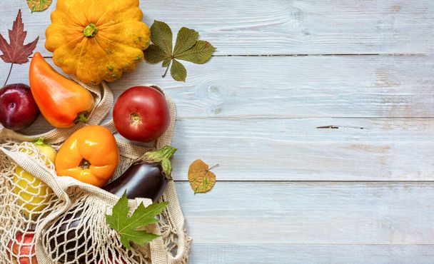 Eco-friendly string bag with seasonal fruits and vegetables on wooden background with leaves.Concept: eco shopping, zero waste, harvest festival. Autumn mood. Flat lay.Copy space for your text. - 写真・画像