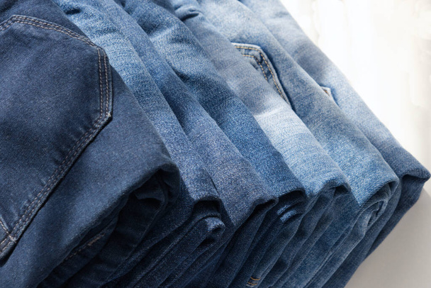 a pile of blue jeans on a light background. Close up. Sunlight. Diagonal - Фото, изображение