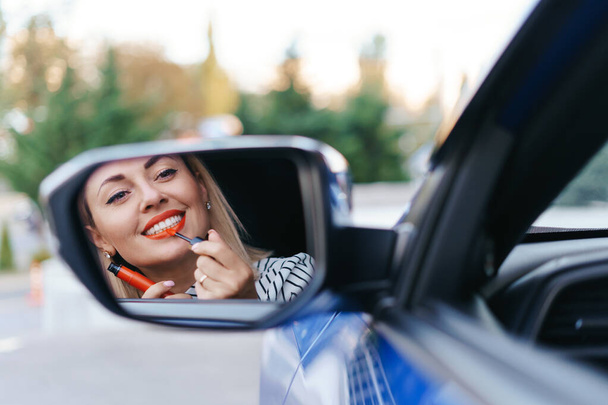 Woman looking in cars side mirror and putting on lipstick - Foto, Imagen
