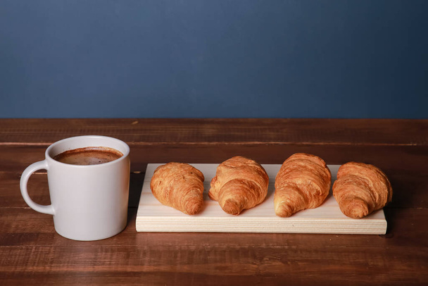 Fresh baked croissants on chopping board, mug of black coffee on brown wooden table. Cup of hot Americano with foam, buns, rolls close up. Food, French breakfast, morning menu, cafe - Foto, afbeelding