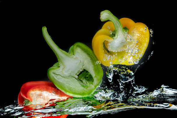 Splattered colored bell peppers splashed on a black background with a cut-out background. - Фото, зображення