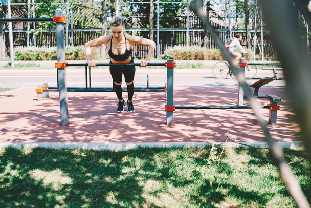 Jeune femme mince en vêtements de sport faire pousser vers le haut exercice sur barre horizontale faire de l'exercice sur le terrain de sport le jour ensoleillé - Photo, image
