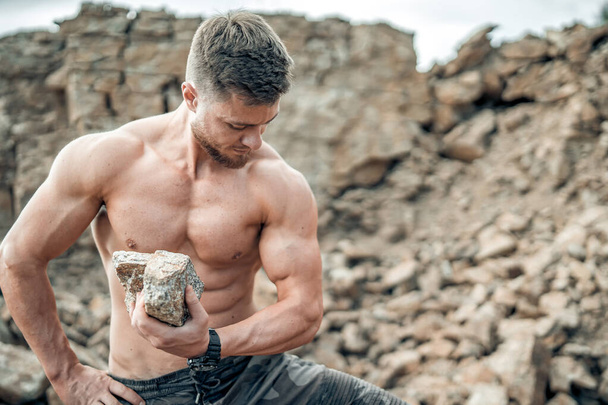 Athletic man sitting on a mountain with heavy rock. Quarry background. Outdoor training concept - Foto, imagen