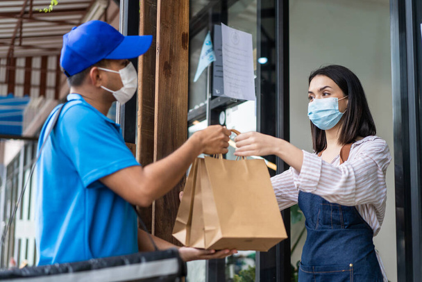 アジアの食品配達人は、 Covid-19パンデミックのために保護マスクを着用し、コーヒーショップのレストラン労働者から飲料注文を受けています。ウエートレスは新しい通常のライフスタイルのための郵便配達人に持ち帰りバッグを与える. - 写真・画像