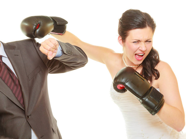 Conflict in relationship concept. Married couple fighting with each other. Woman wearing wedding dress and boxing gloves punching her husband in elegant suit. - Photo, Image