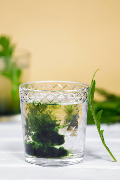 Zielony napój chlorofilu w szklance z kroplami wody na białym stole, pomarańczowe tło. Żywność i napoje przeciwutleniające, Dieta Detox - Zdjęcie, obraz