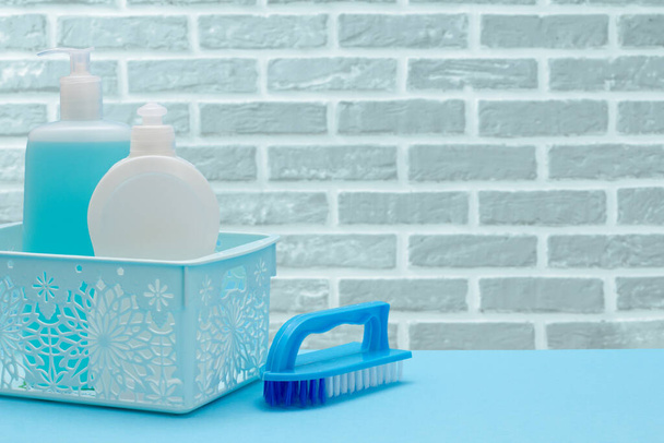 Botellas de líquido lavavajillas en cesta y cepillo sobre fondo de pared de ladrillo. - Foto, imagen