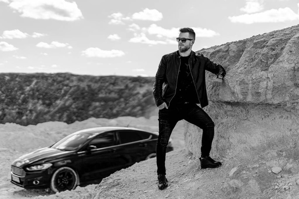 Handsome man standing on the road near opened door of his car. Transportation concept. Black and white photo - Valokuva, kuva
