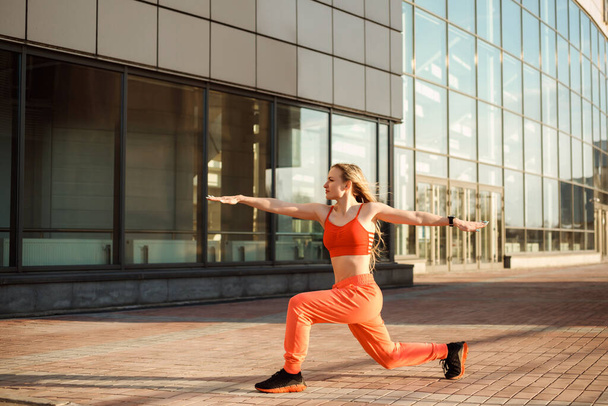 Attractive woman is practicing yoga, standing in warrior two pose in front of the urban building. - Foto, Bild