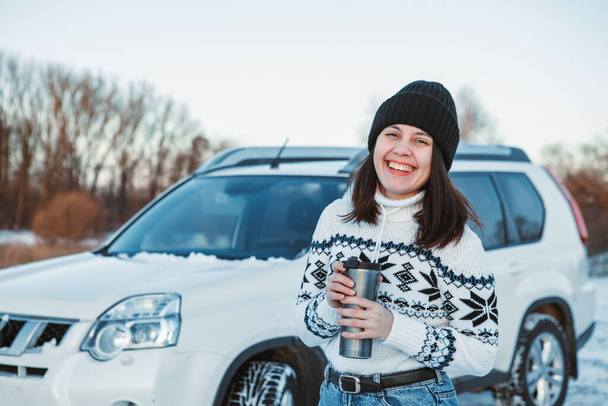 Porträt einer lächelnden Frau mit einem Becher im winterlichen Outfit Geländewagen auf dem Hintergrund Kopierraum - Foto, Bild