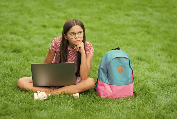back to school. teen girl use computer on green grass in park. child with backpack and notebook. new technology in modern life. study. unhappy thinking kid working on laptop. online education - Foto, imagen