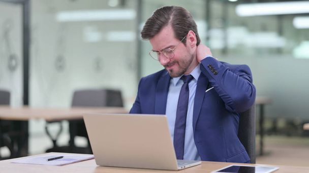 Stanco giovane uomo d'affari con computer portatile con dolore al collo in ufficio  - Foto, immagini