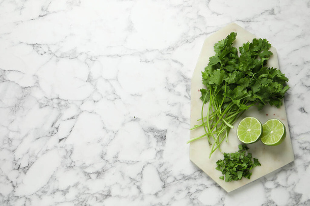 Fresh green cilantro and lime on white marble table, top view. Space for text - Fotografie, Obrázek