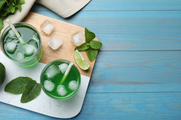Delicious mint liqueur with green leaves and ice cubes on turquoise wooden table, flat lay. Space for text - Fotó, kép
