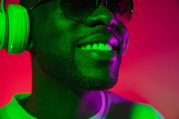 Creative image of African young man in casual clothes isolated on red color studio background in neon light, filter. Concept of human emotions, facial expression, youth, feelings, ad. - Fotografie, Obrázek