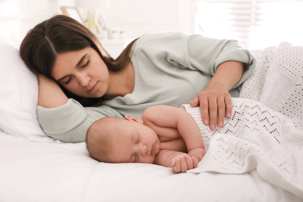 Young mother resting near her sleeping baby on bed at home - Foto, imagen