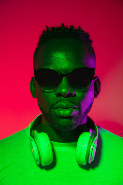 Creative image of African young man in casual clothes isolated on red color studio background in neon light, filter. Concept of human emotions, facial expression, youth, feelings, ad. - Foto, afbeelding
