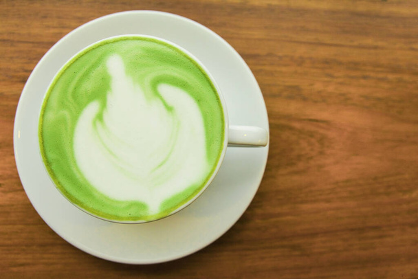 Top viwe. Melk groene thee latte in kopje op hout achtergrond - Foto, afbeelding
