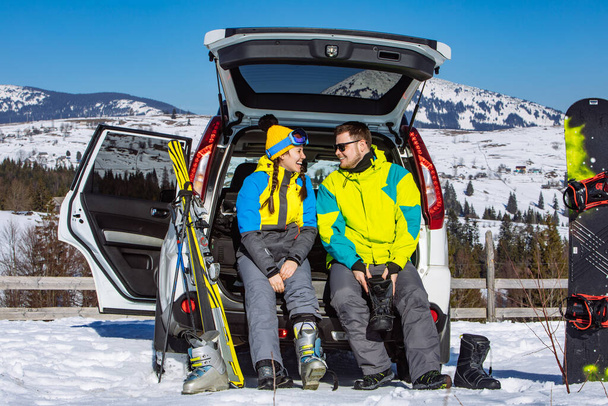 mężczyzna i kobieta ubierający się w sprzęt narciarski w pobliżu samochodu SUV. góry na tle - Zdjęcie, obraz