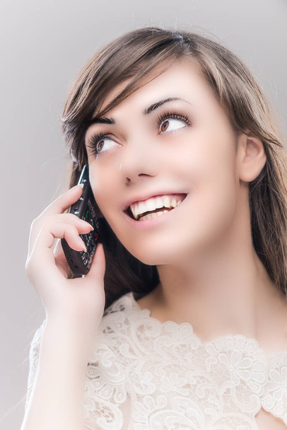 Una joven hermosa mujer riendo con el pelo largo y oscuro hablando en un teléfono celular sobre un fondo gris. - Foto, imagen