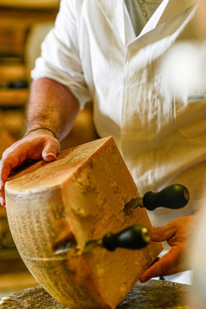 PARMA, ITALY - Jan 18, 2021: A cheese maker cutting parmesan cheese wheel into quarters - Fotó, kép