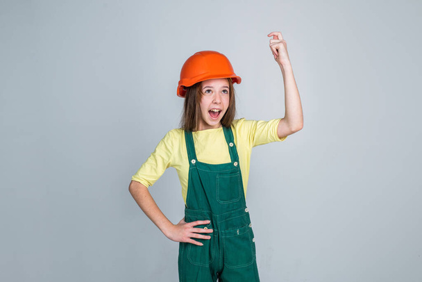teen girl laborer in protective helmet and uniform on grey background, success - Φωτογραφία, εικόνα