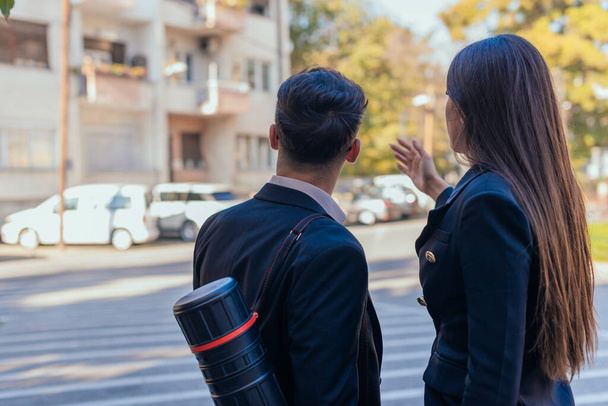Backview of suited male and female architects looking together at a building blueprint outside - Photo, Image