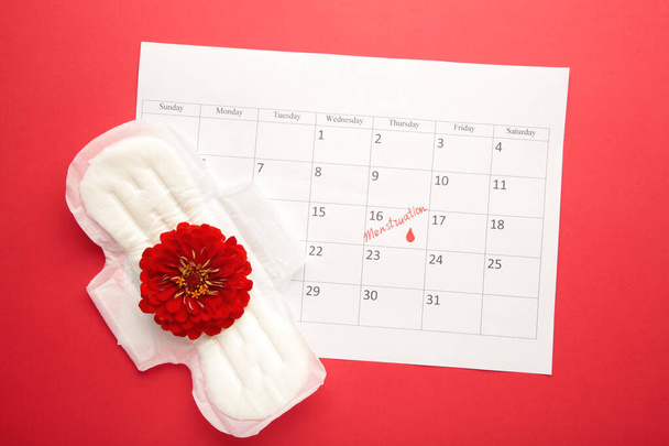 Menstruation calendar with pads on red background. Woman critical days, woman hygiene protection. Top view - Photo, Image