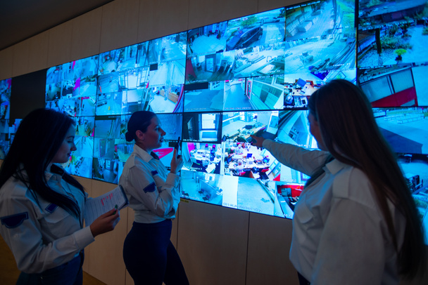 Guardias de seguridad de pie frente a un gran monitor de CCTV en la sala de control principal mientras leen y discuten los planes - Foto, imagen