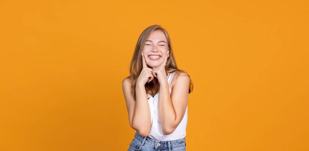 Продолжай улыбаться. Веселая молодая девушка улыбается на оранжевой пекарне - Фото, изображение
