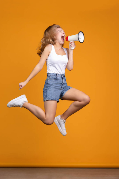 Animadora foto de saltar y gritando joven modelo femenino sobre fondo naranja - Foto, Imagen