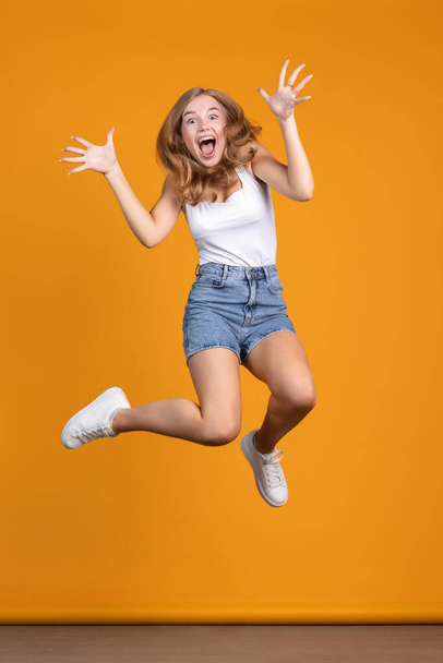 Sorpresa. Felice e allegra giovane donna che salta e ride su sfondo arancione - Foto, immagini